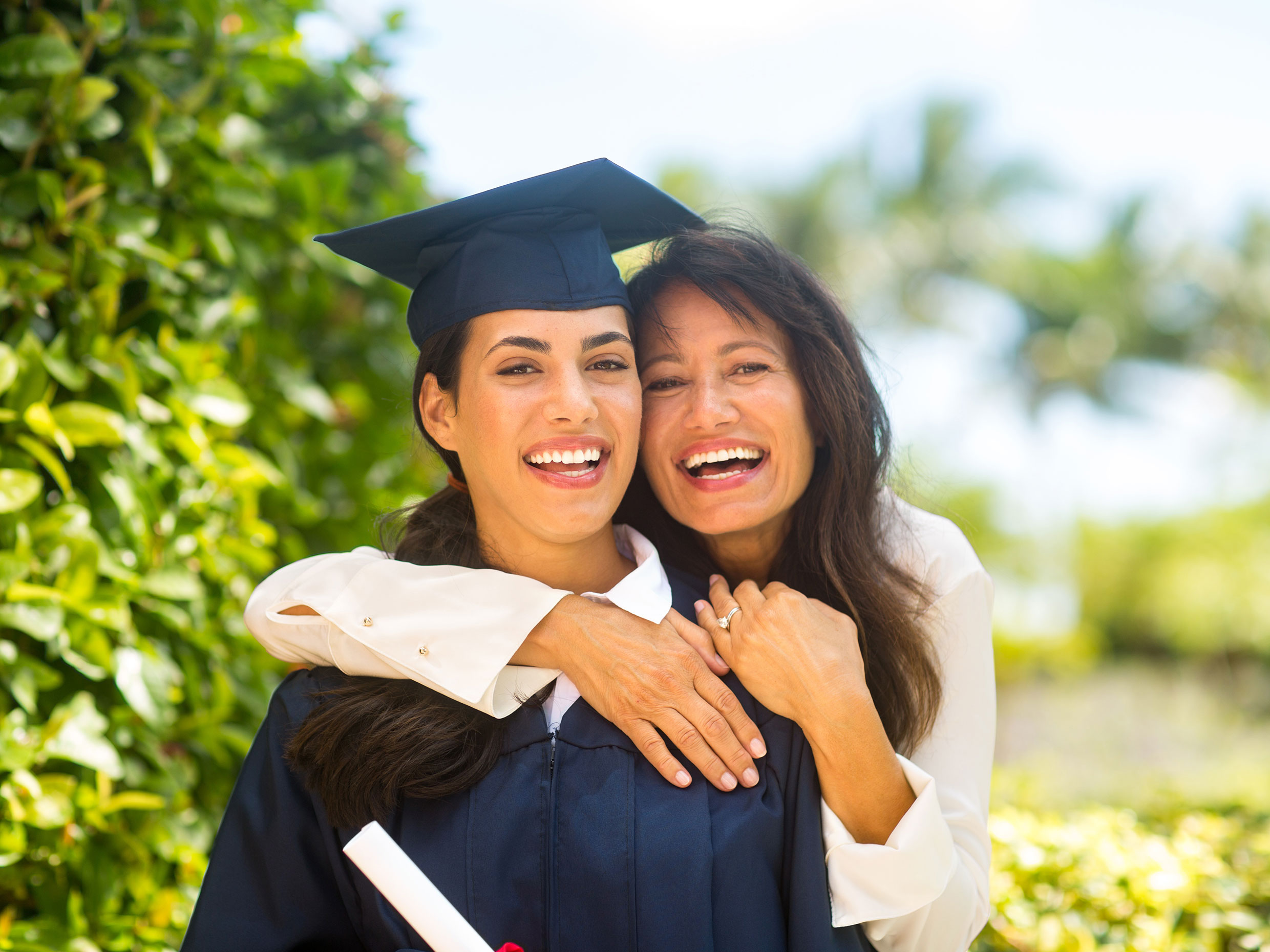 Smiling student in graduation cap and gown standing beside mother.