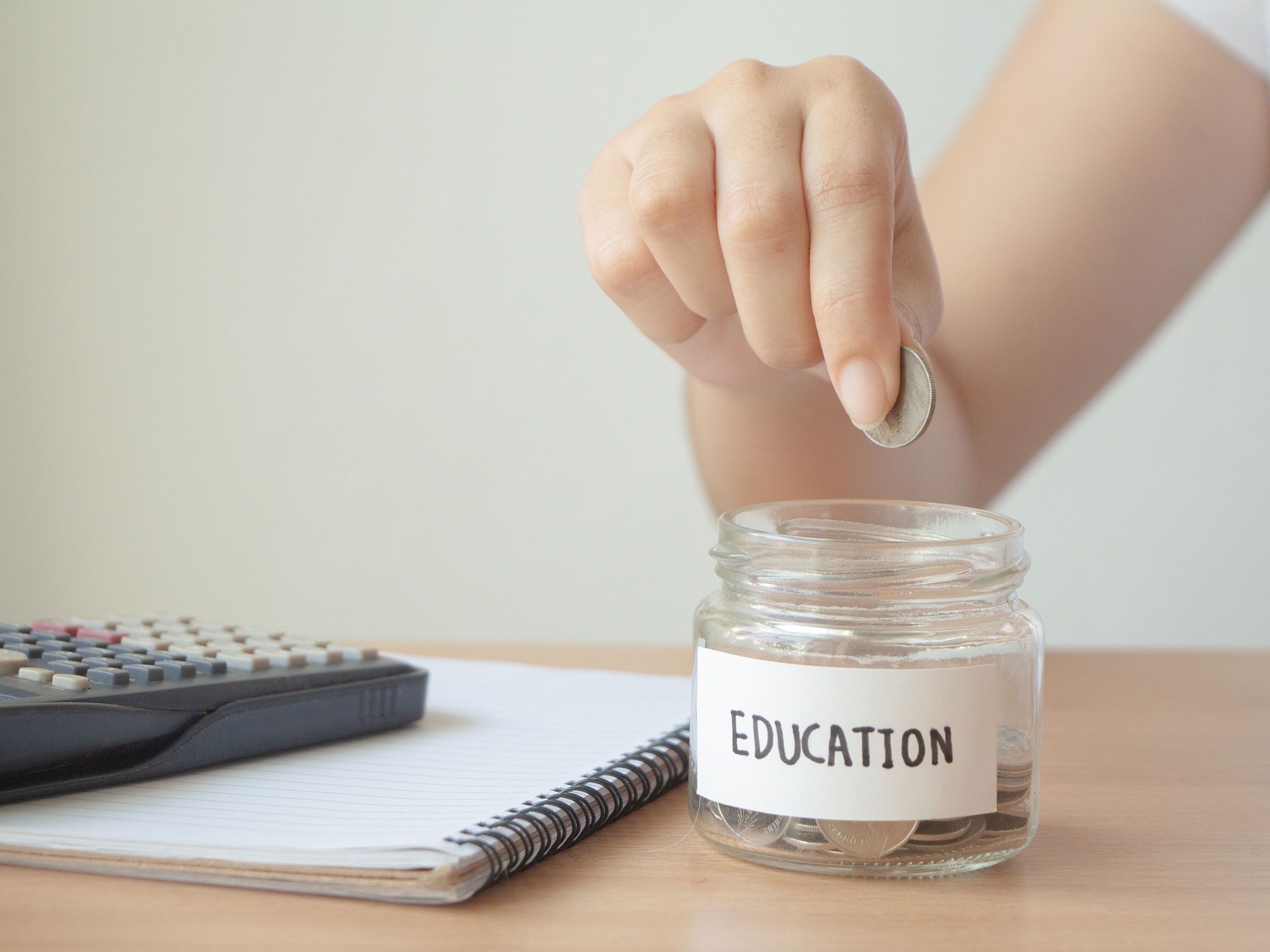 Hand dropping coin into jar labelled 'Education.'