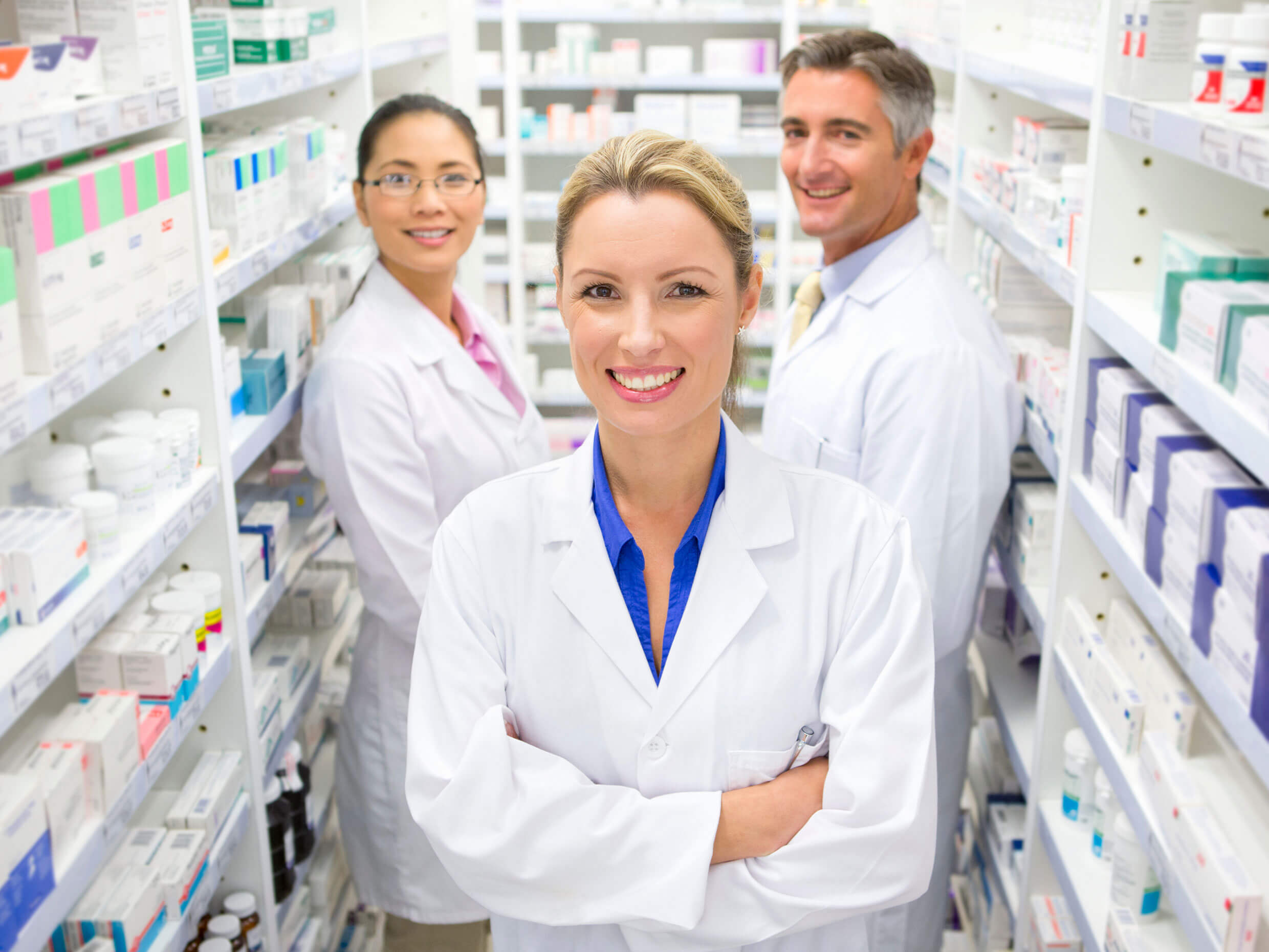 A Pharmacy Assistant confidently standing with a licensed Pharmacist and a Pharmacy Technician in their workplace, a retail pharmacy
