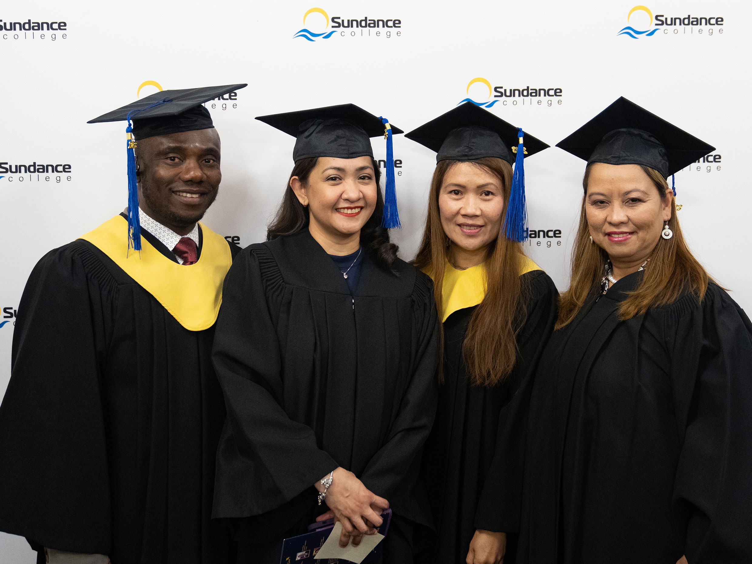 Four smiling alumni standing in front of the white signboard with the Sundance College logos during the 2023 graduation ceremony in Calgary.