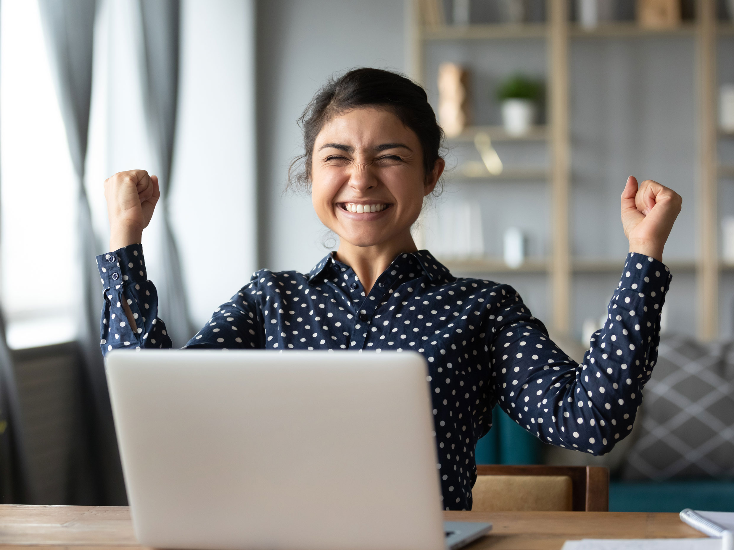 Woman sitting at computer, cheering with arms in the air.