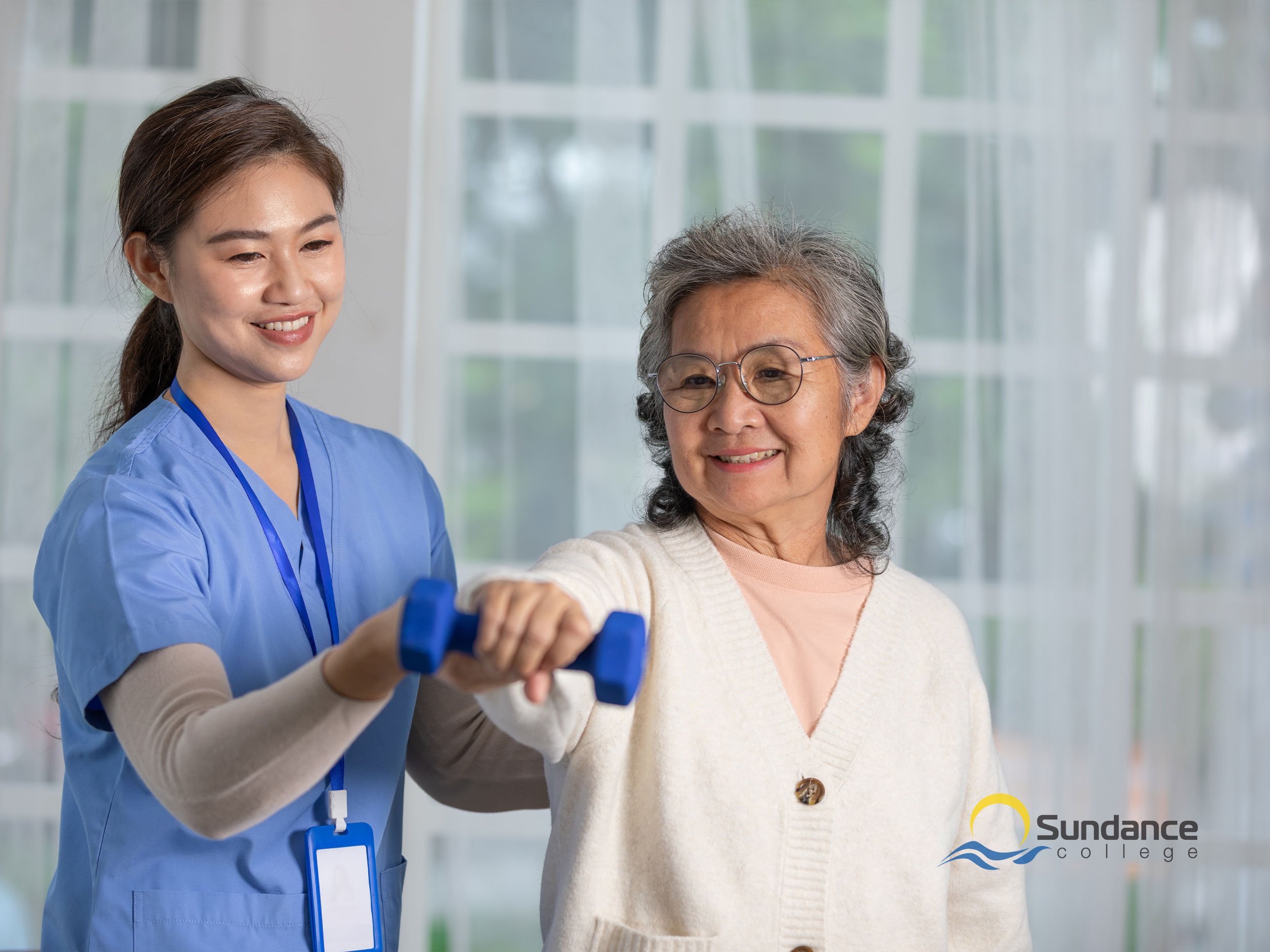 young female personal support care worker helping an old lady lift weights as she does physical mobility exercises
