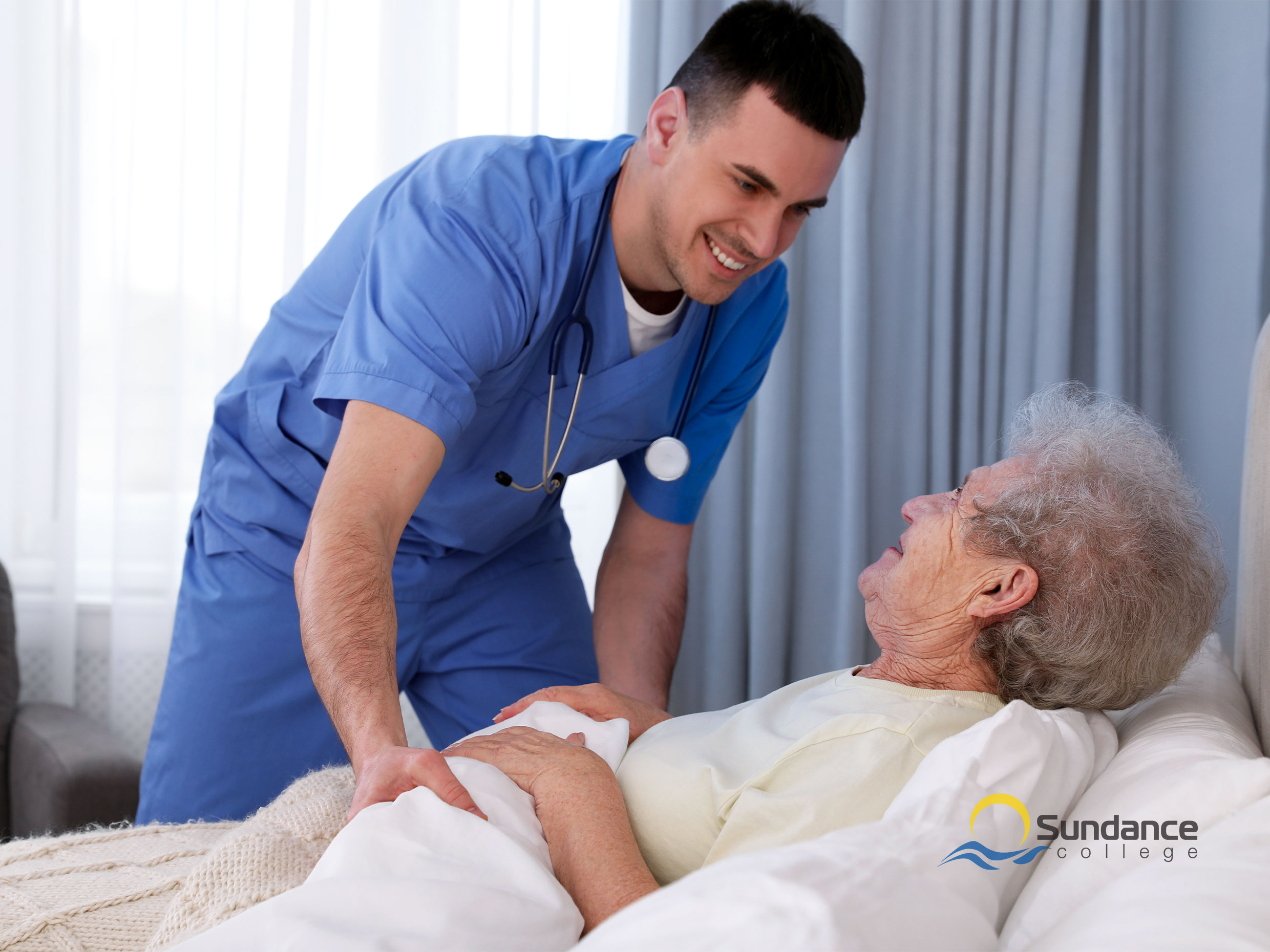 Young male personal support care worker in blue scrubs tucking an old lady into bed in her home or nursing home