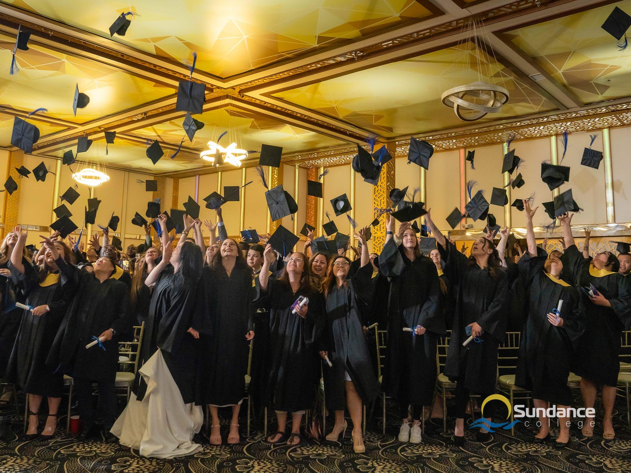 accounting diploma graduates in graduation gowns from Sundance College, throwing graduation caps in air joyfully