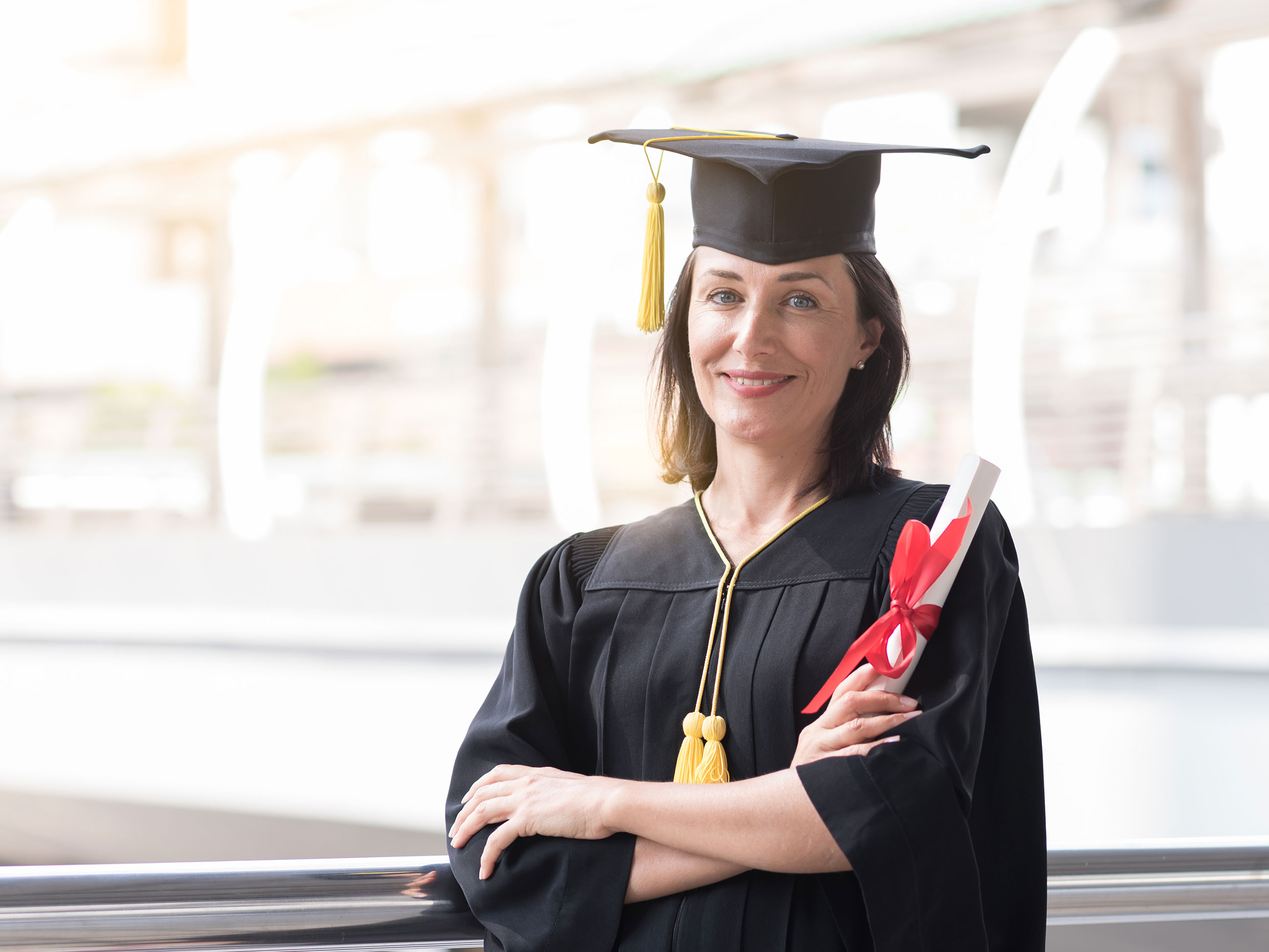 career college graduand smiling in graduation gown and graduation cap while holding a career college diploma