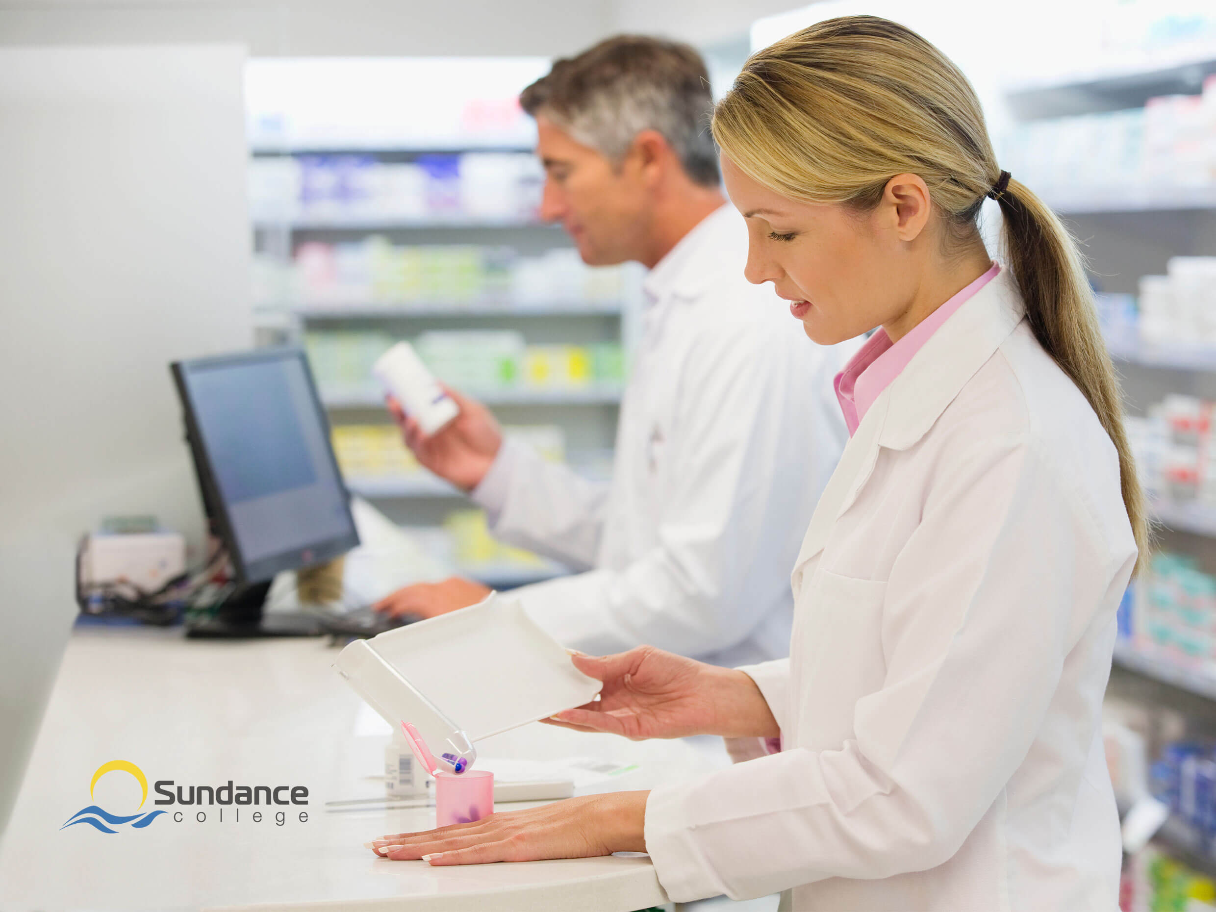 Pharmacy Assistant checking labels and inventory while a Pharmacy Technician refills a bottle in a retail pharmacy