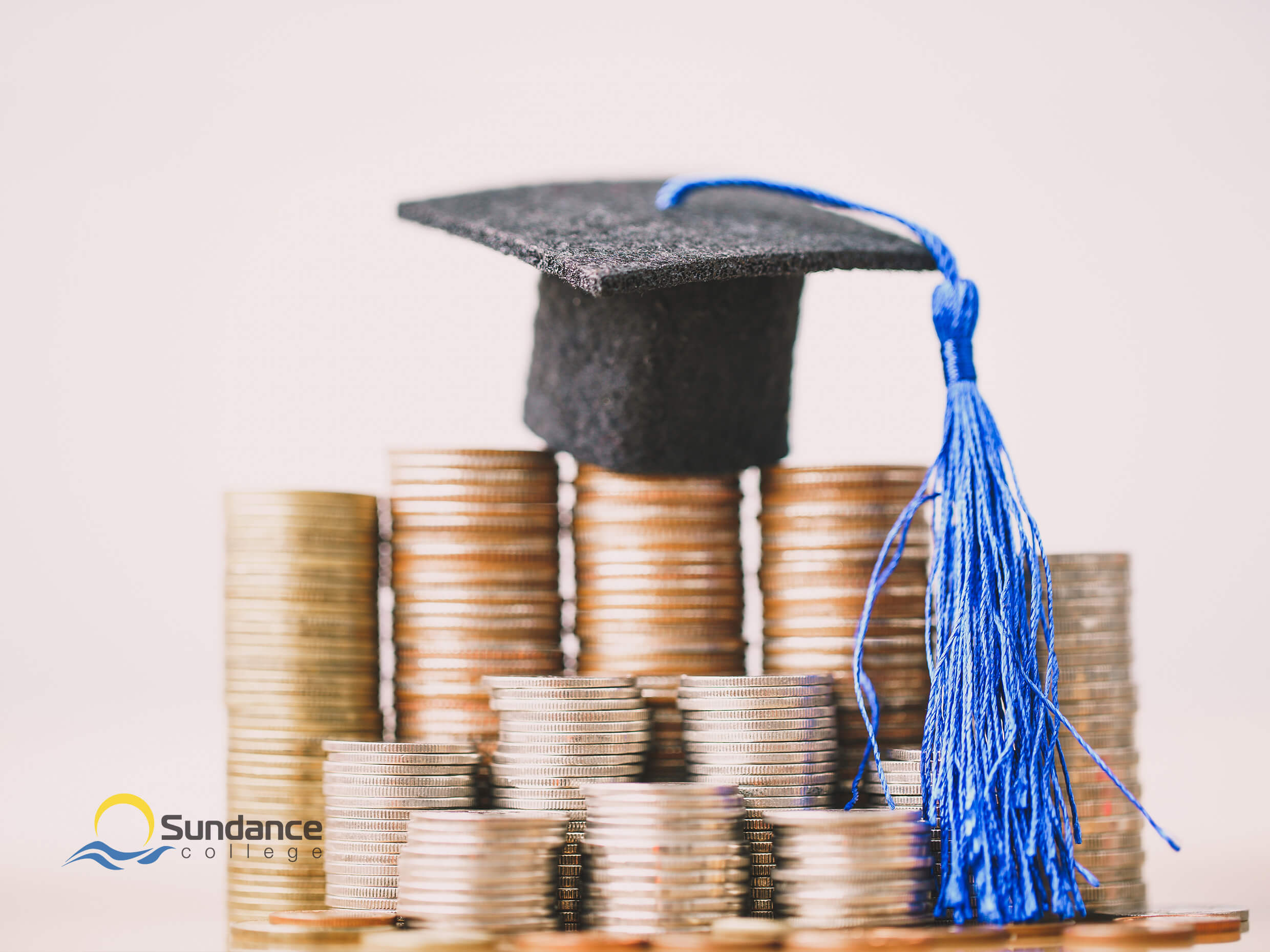 A closeup of a miniature graduation cap sitting on a stack of coins, symbolizing the value payroll administrators provide to organizations through their payroll diploma