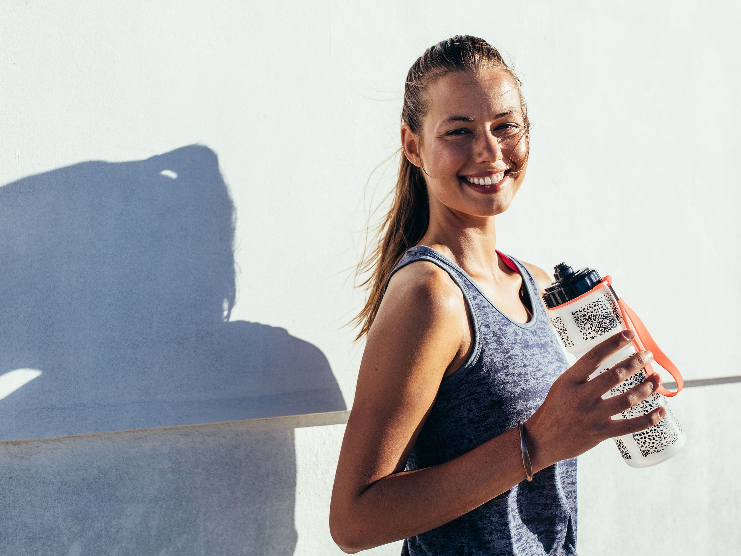 woman smiling while wearing an exercise shirt and holding a water bottle