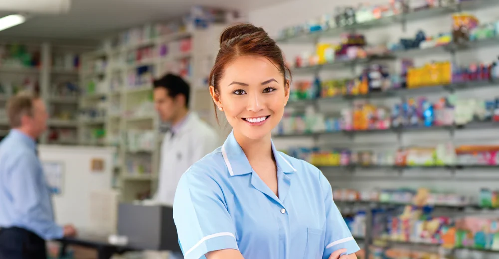 Female pharmacy assistant standing in front of a pharmacy backdrop.