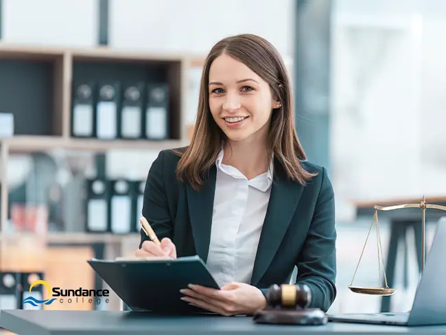 Smiling woman in professional attire at a law office desk, reviewing documents — suggesting a legal administrative job.