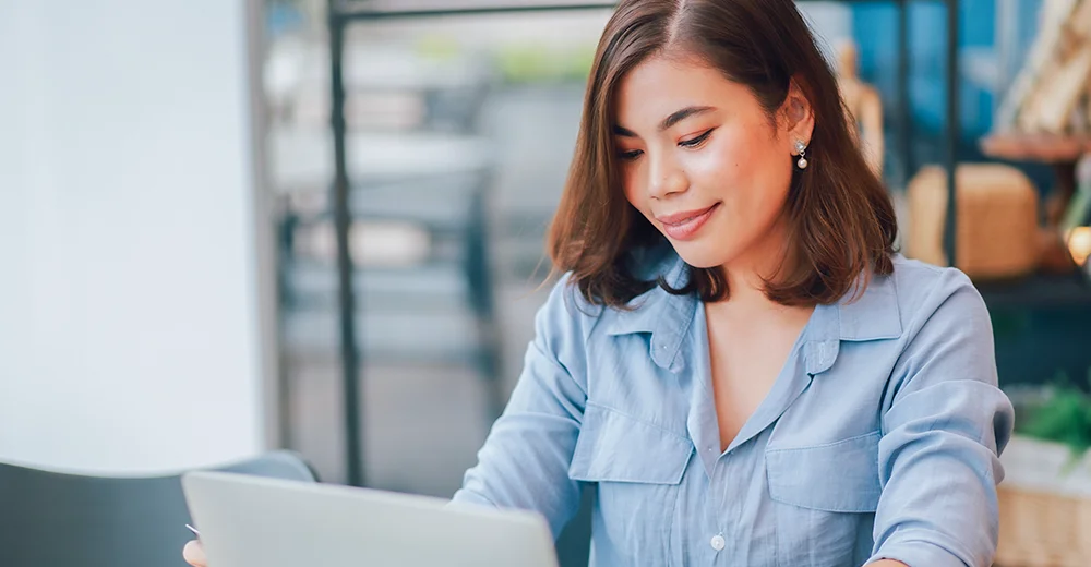 A young woman sitting with her laptop, reviewing a resume on the screen.