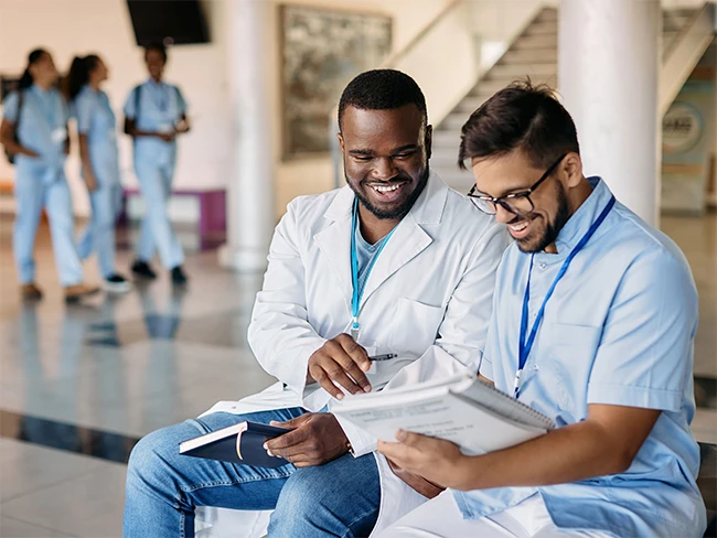 Man in lab coat smiling and reviewing notes presented by man in scrubs.