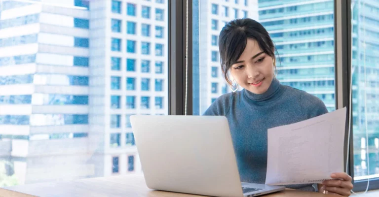 a woman sitting at a desk looking at a paper digital marketing portfolio desktop