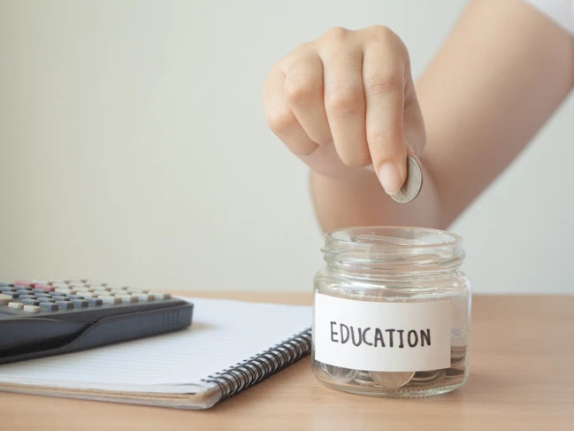 a hand putting a coin into a jar savings money student