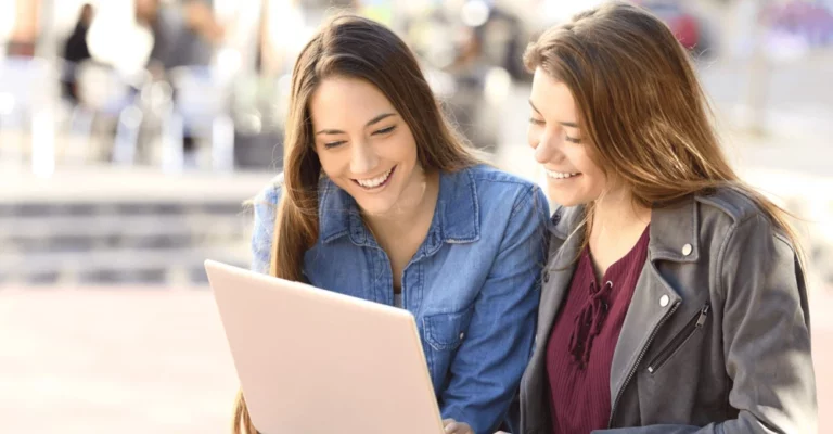 two female students outside college looking laptop hero image