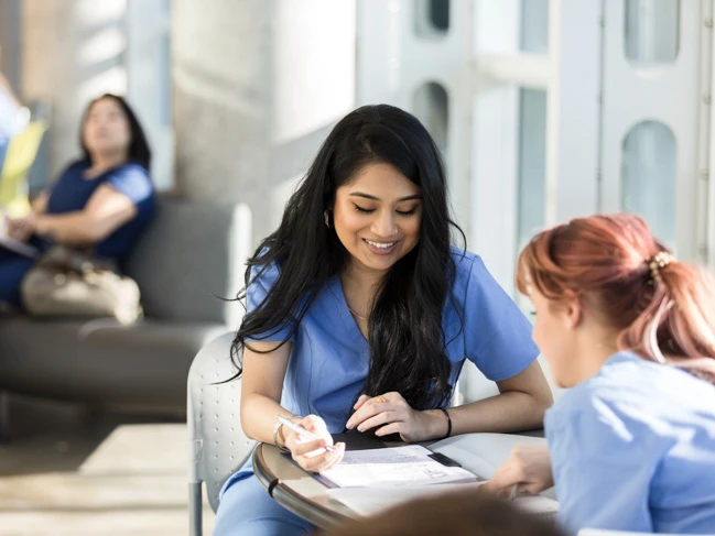 a woman in blue scrubs sitting at a table with other people in the background