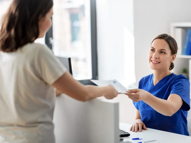 Medical assistant handing paperwork to patient