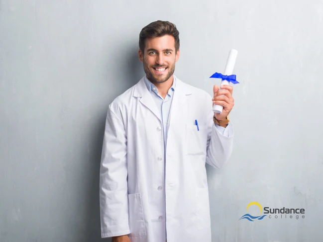 pharmacy assistant over grey wall holding diploma