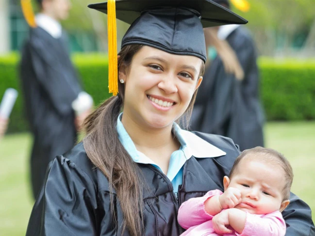 a woman in a graduation gown holding a baby