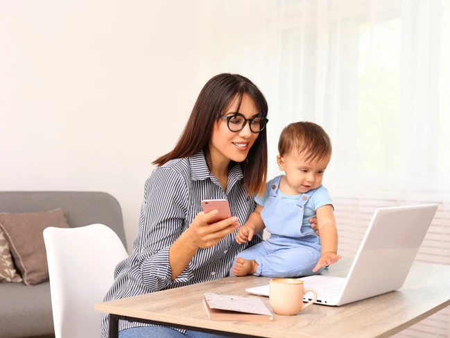 a woman sitting with her kid working on a laptop