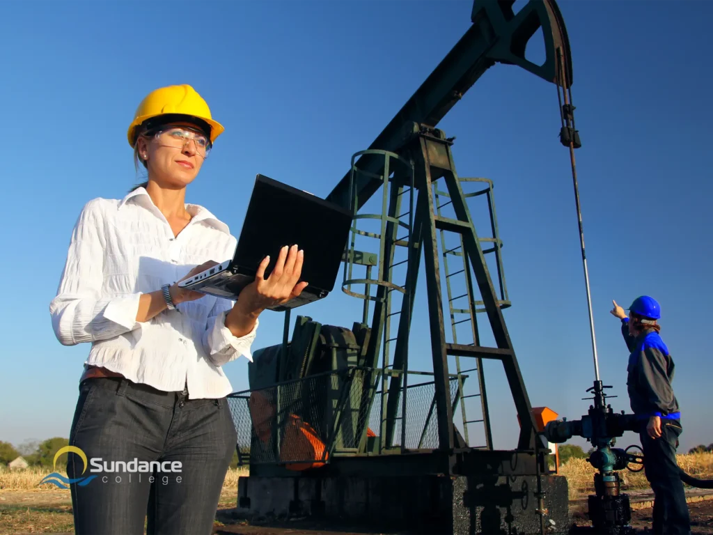 female oil and gas administrator standing in front of an oil extraction site holding a laptop.