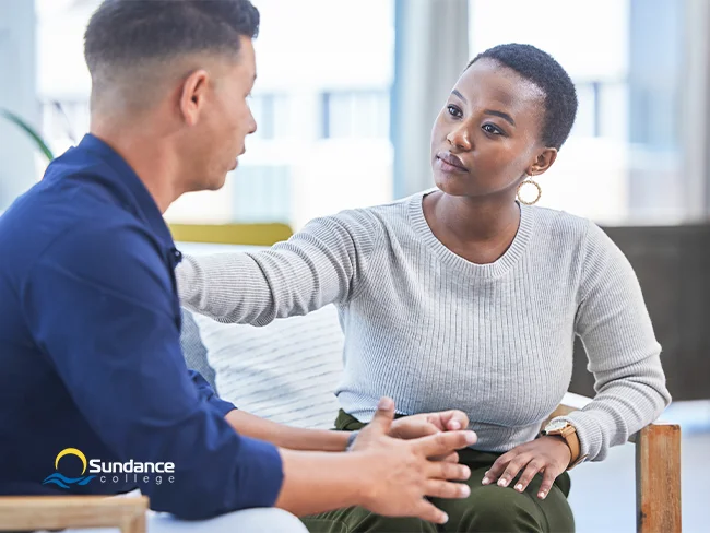 Addictions and community health worker providing one-on-one support to a client. Her hand is resting on his shoulder as she listens carefully to him.