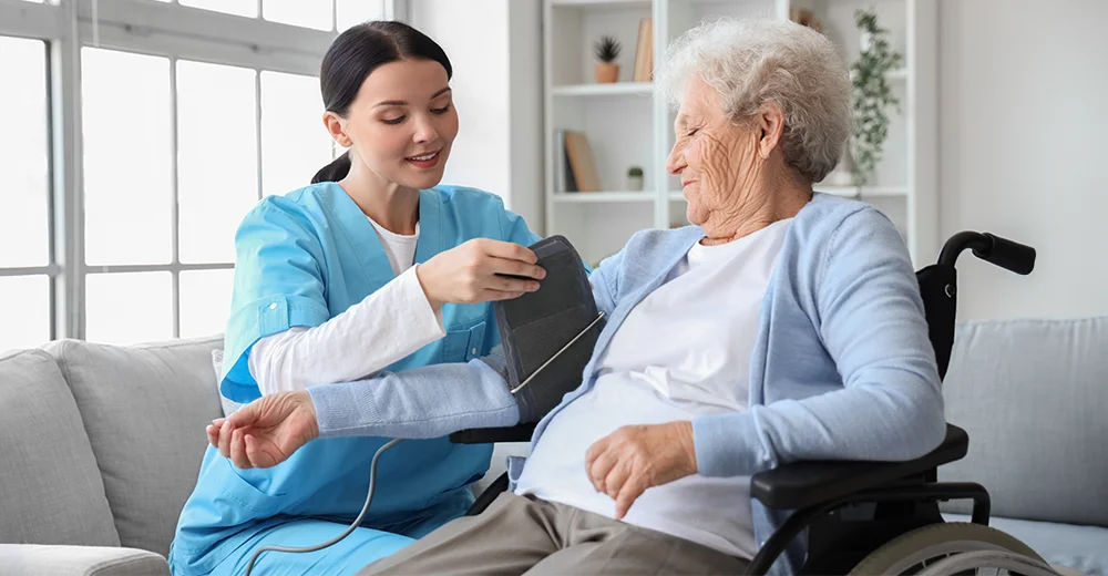 A personal support worker carefully wraps the right arm of an elderly woman in a wheelchair with a blood pressure cuff.