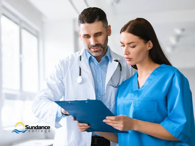 Medical Office Assistant engaging in a discussion with a doctor. They are both looking at a clipboard in a hospital setting.