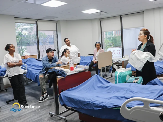 Training in action at Sundance College’s Edmonton campus, featuring five students engaged in learning with an instructor who is explaining the fundamentals of personal support work.