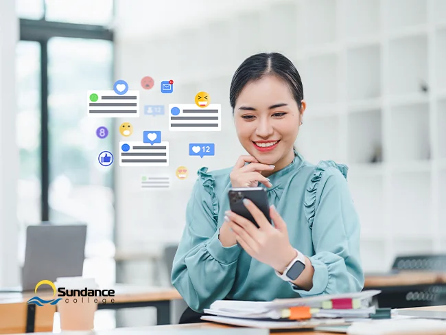 Young female social media manager seated at her desk, checking her phone to monitor engagement and respond to audience interactions.