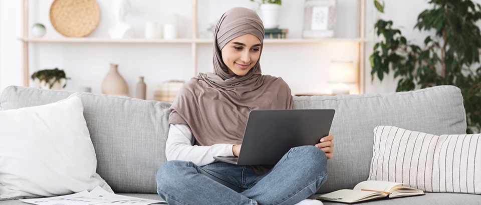 Student sitting on sofa with laptop on her lap.