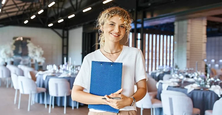 Woman holding clipboard in elegant event venue, likely an event planner.
