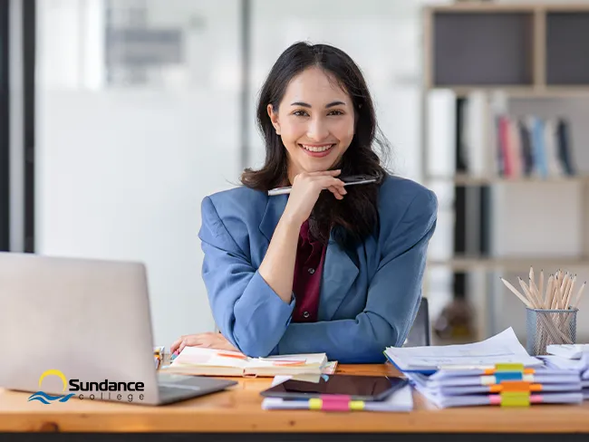A smiling woman works at her desk with a laptop and documents, celebrating her career training success.
