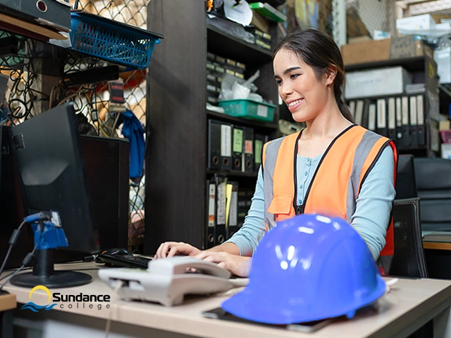 Woman in safety vest and hard hat holding clipboard at oil and gas facility, representing oil and gas admin careers.