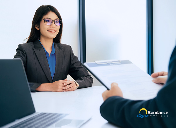 A woman smiles while a man reviews her resume, an example of an HR management interview.