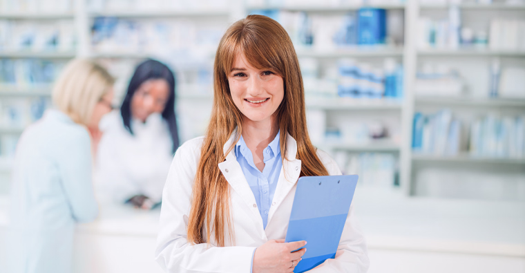 A woman holds a clipboard while working in a pharmacy. An example of starting a new career as a pharmacy assistant after choosing the right pharmacy assistant program.