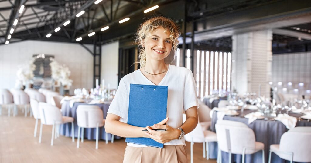 Woman holding clipboard in elegant event venue, likely an event planner.