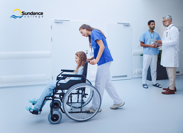 Personal Support Worker pushing a child in a wheelchair through a healthcare setting.