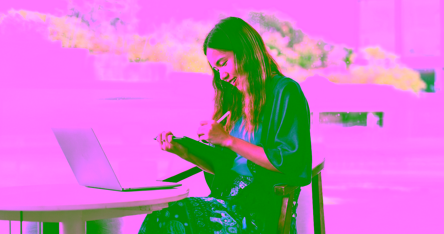 A young woman smiles as she works on a tablet in an outdoor cafe.