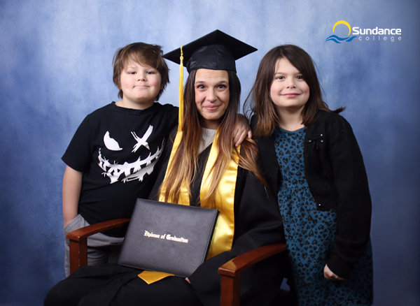 Sundance College graduate and student mom, Jessica M., holding her diploma certificate with her two children.