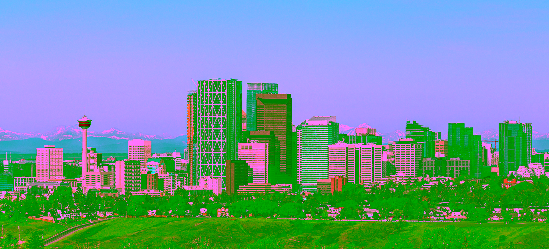 A panoramic view of the Calgary skyline, featuring downtown skyscrapers, the Calgary Tower, and the snow-capped Rocky Mountains in the distant background, showcasing the location of Sundance College Calgary campus.