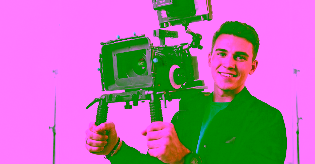 A smiling videographer looks into the viewfinder on his camera.