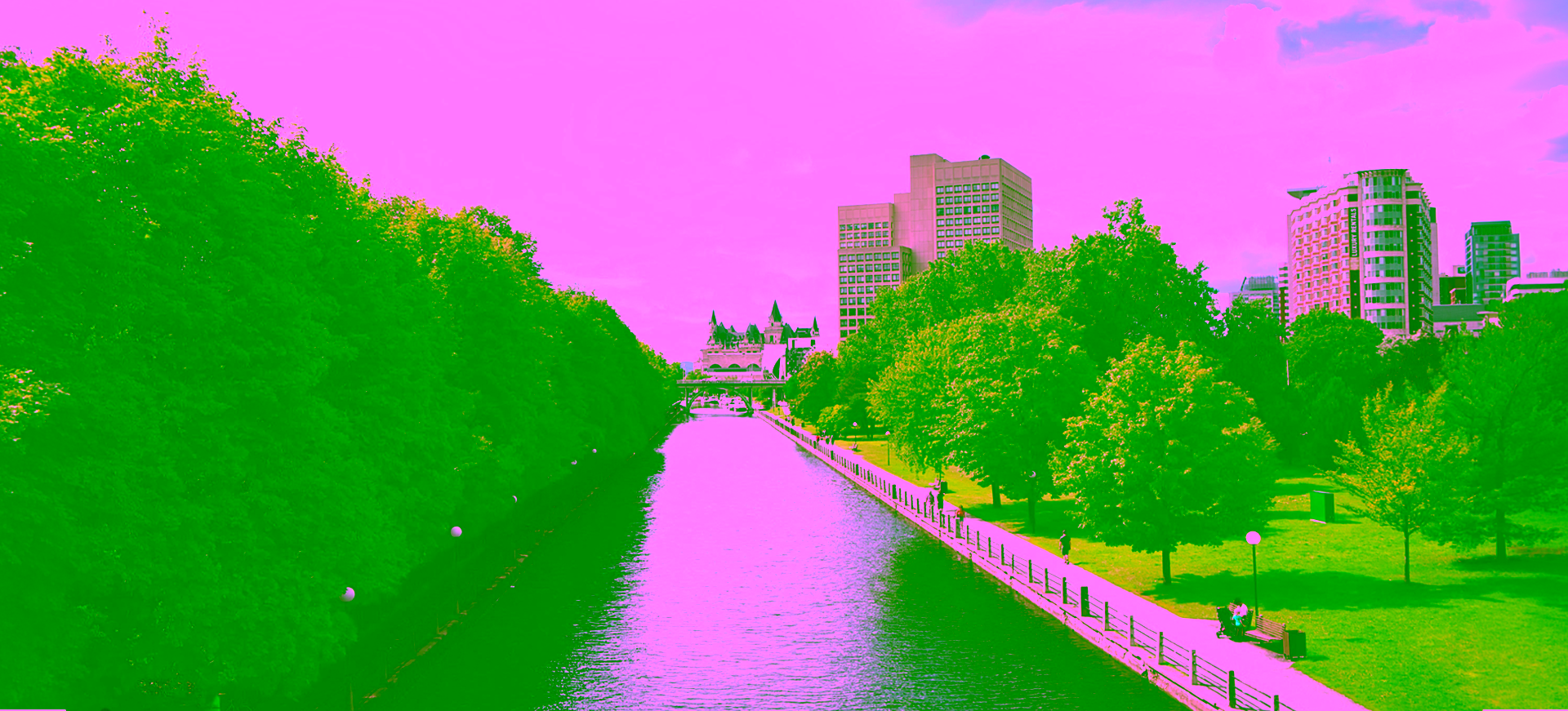 A high-angle view looking down the straight waters of the Rideau Canal in Ottawa, Ontario, on a bright day with fluffy white clouds.