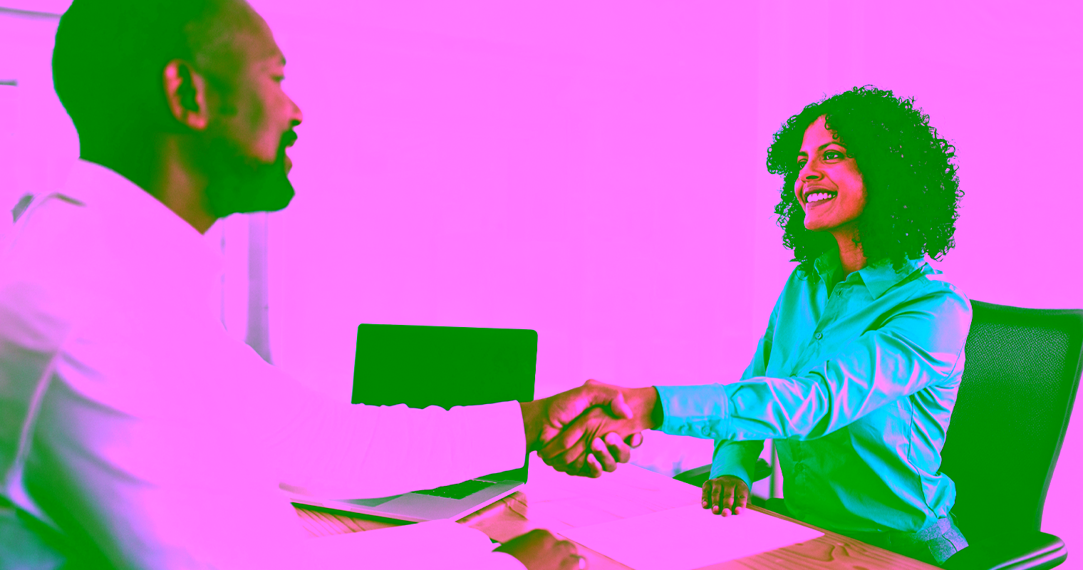 A male job candidate shakes hands with a female HR professional in an office setting.
