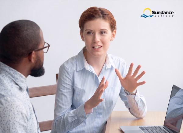 A female HR manager at her desk discussing a workplace concern with a male.