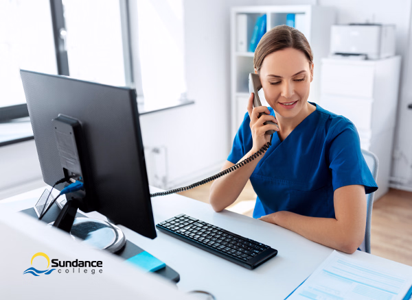 A female medical receptionist on a call at her desk while going through documents.