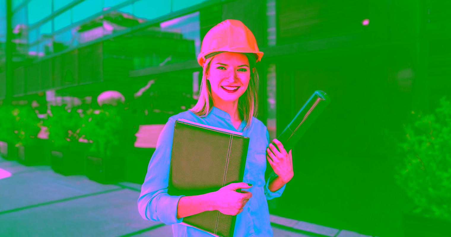 An Architectural Building Technologist wearing a hard hat stands in front of a building holding a clipboard and blueprint.