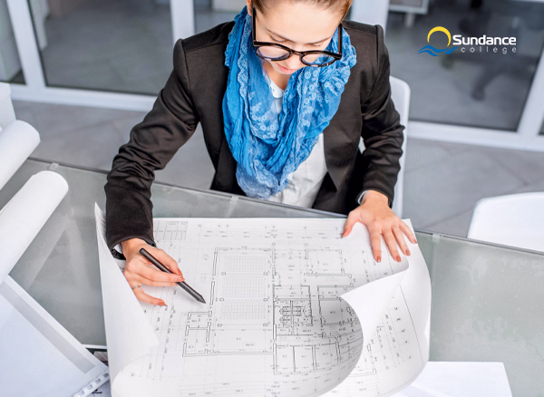 An architectural building technologist makes notes on a building blueprint.
